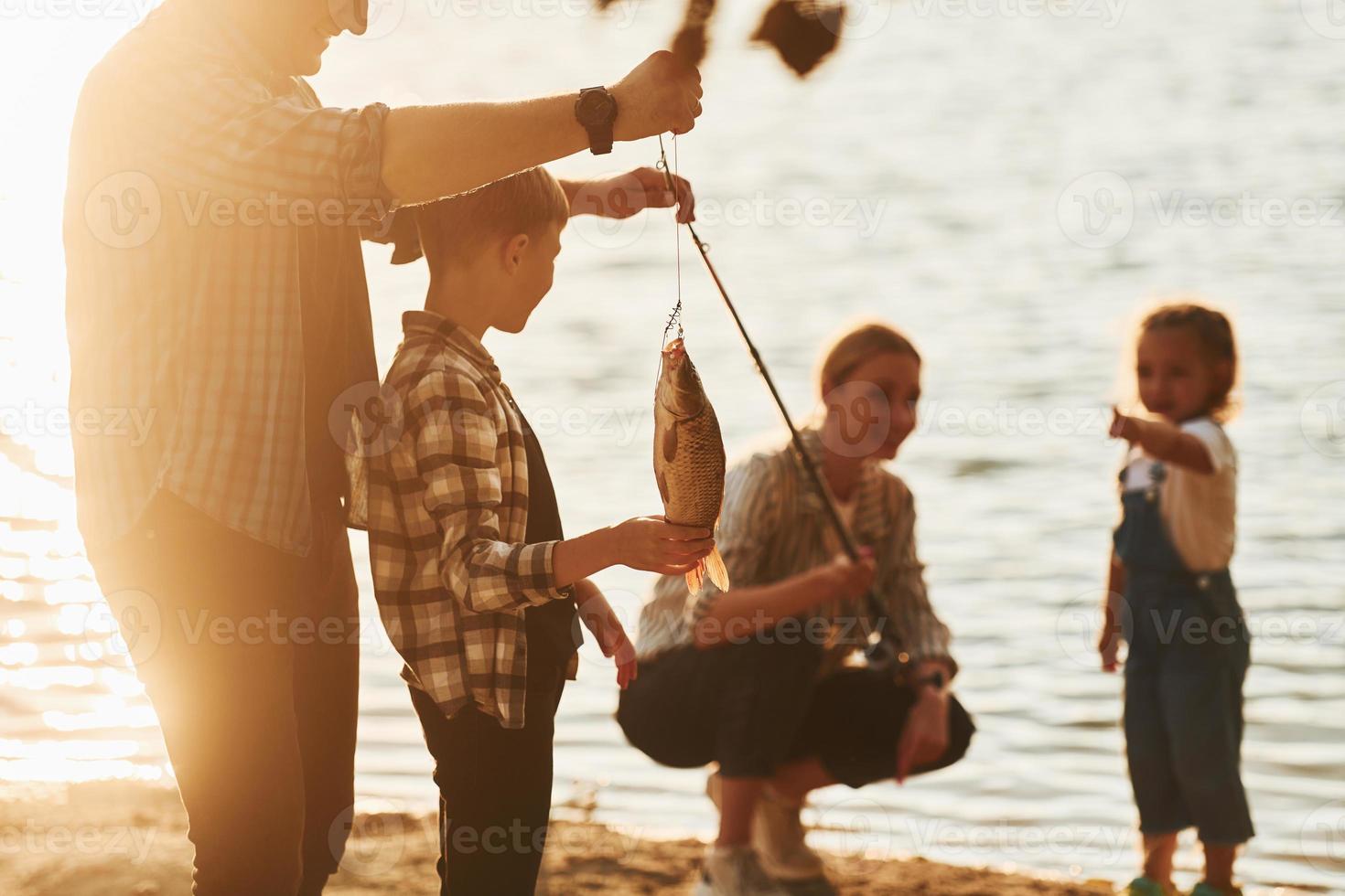 i tillfällig kläder. far och mor med son och dotter på fiske tillsammans utomhus på sommartid foto