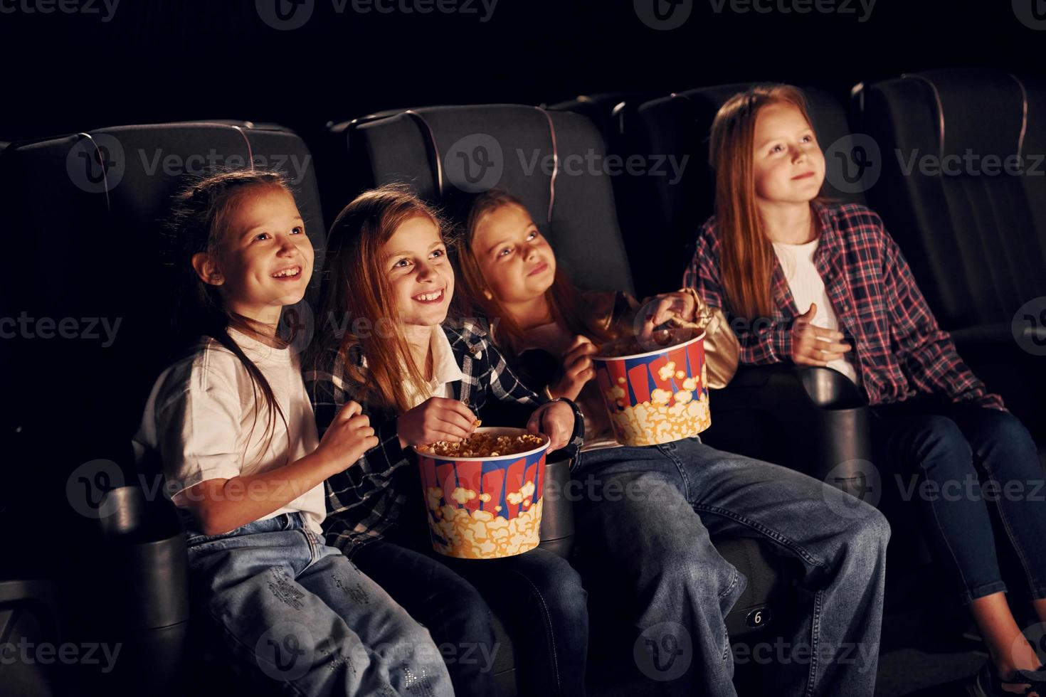 avkopplande och har roligt. grupp av barn Sammanträde i bio och tittar på film tillsammans foto