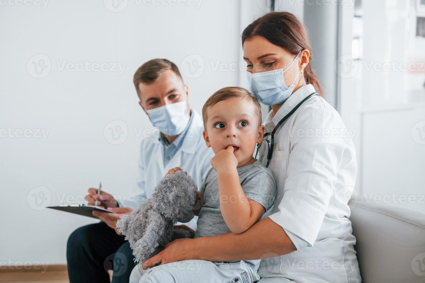 liten pojke är i de klinik. två doktorer i vit rockar är i de sjukhus arbetssätt tillsammans foto