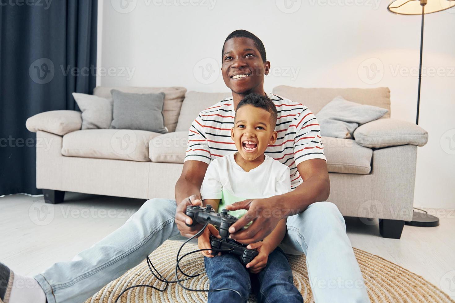 använder sig av styrspakar till spela video spel. afrikansk amerikan far med hans ung son på Hem foto