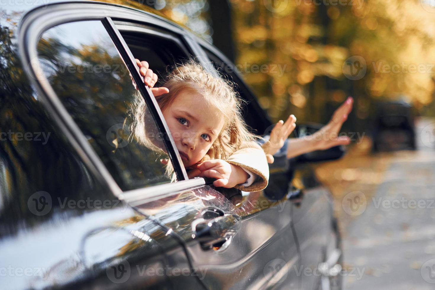 liten flicka med henne bror Sammanträde i de bil och ser genom de öppnad fönster foto