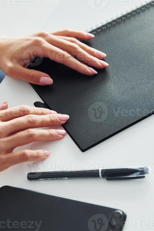 kvinnas händer innehav svart färgad anteckningsblock den där liggande på de tabell foto