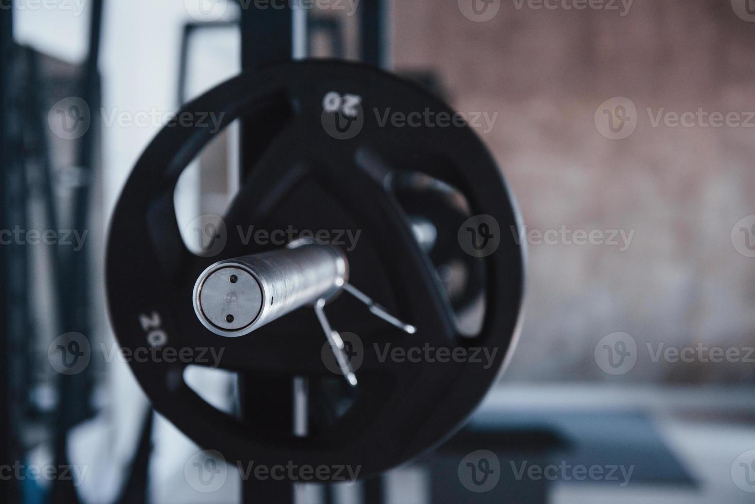 fokuserade på de silver- färgad del av skivstång. svart skivstång på de metall stå i de Gym på dagtid. Nej människor runt om foto