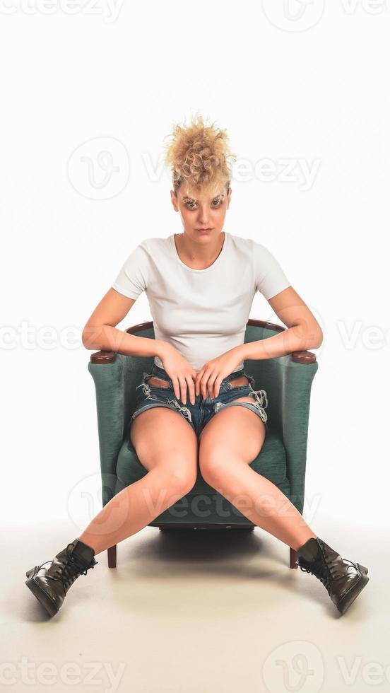 modern eleganta galen blond kvinna lokaliserings i de stol och Framställ i främre av kamera i studio. mode skönhet begrepp. foto