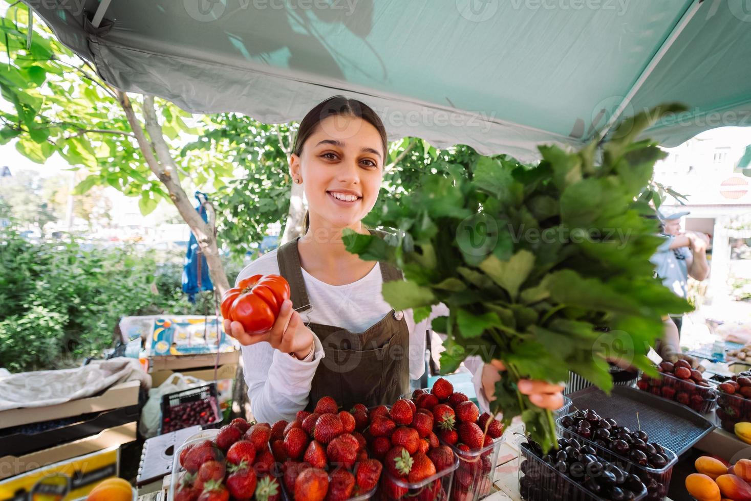 ung försäljare på arbete, innehav persilja och tomat i händer foto
