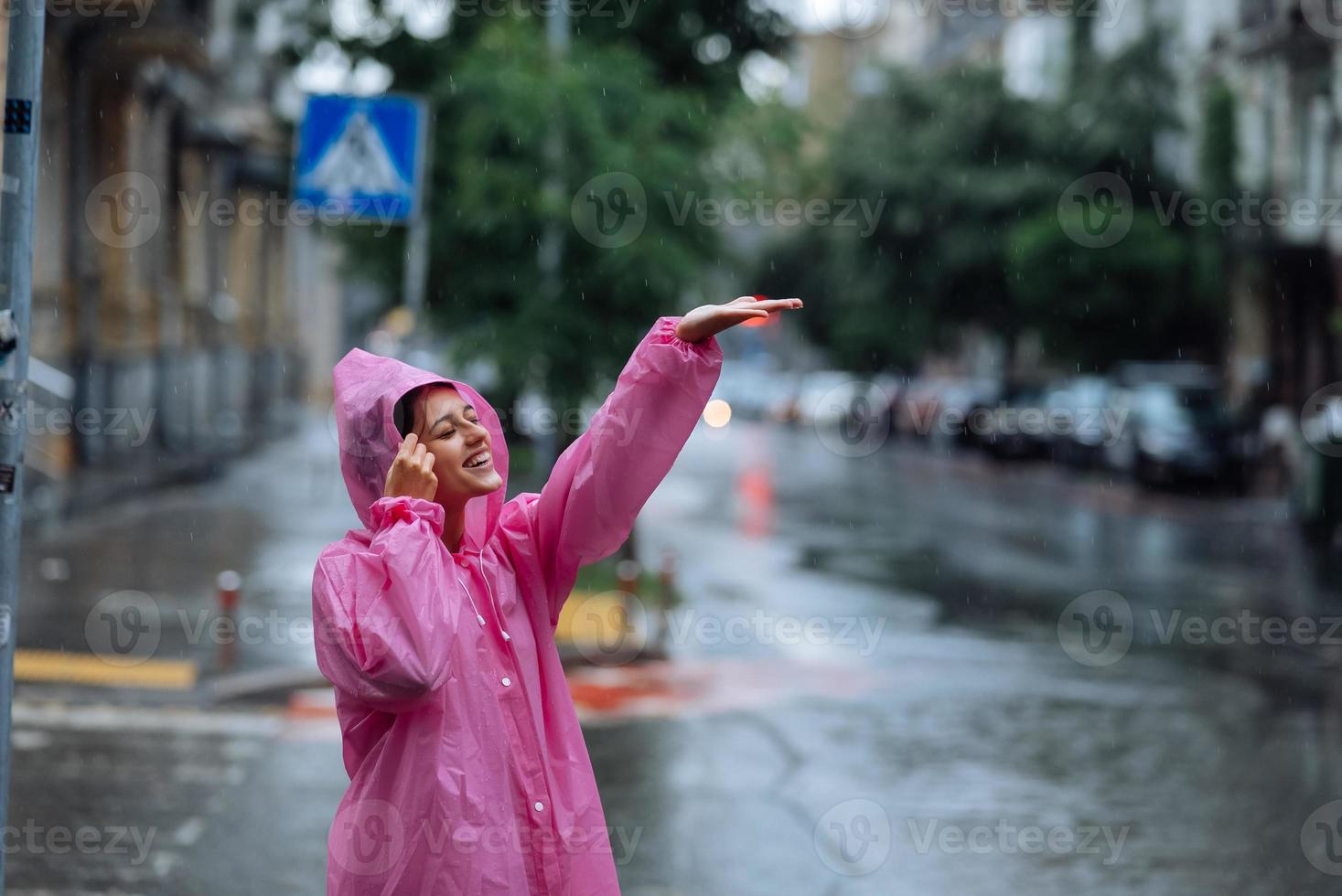 ung leende kvinna med regnkappa medan njuter en regnig dag. foto