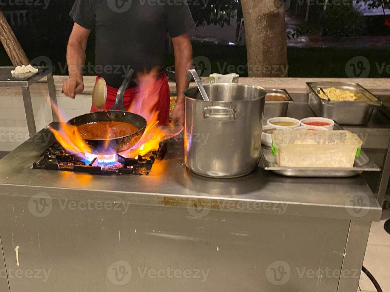 kock, laga mat matlagning i en fräsning panorera på brand mat i en restaurang i ett öppen kök i ett all inclusive hotell i en turistiska värma tropisk Land paradis tillflykt på semester foto