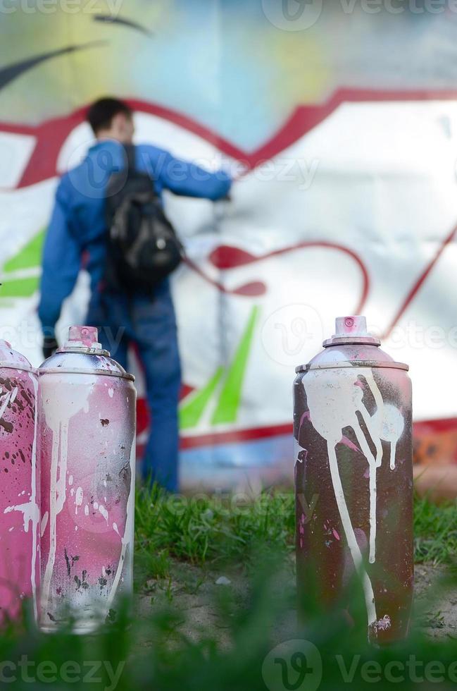 en få Begagnade måla burkar mot de bakgrund av de Plats med de vägg på som de ung kille drar en stor graffiti teckning. modern konst av teckning väggar i graffiti foto