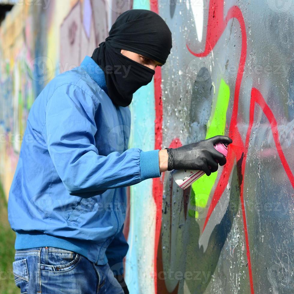 en ung ligist med en dold ansikte målarfärger graffiti på en metall vägg. olaglig vandalism begrepp foto