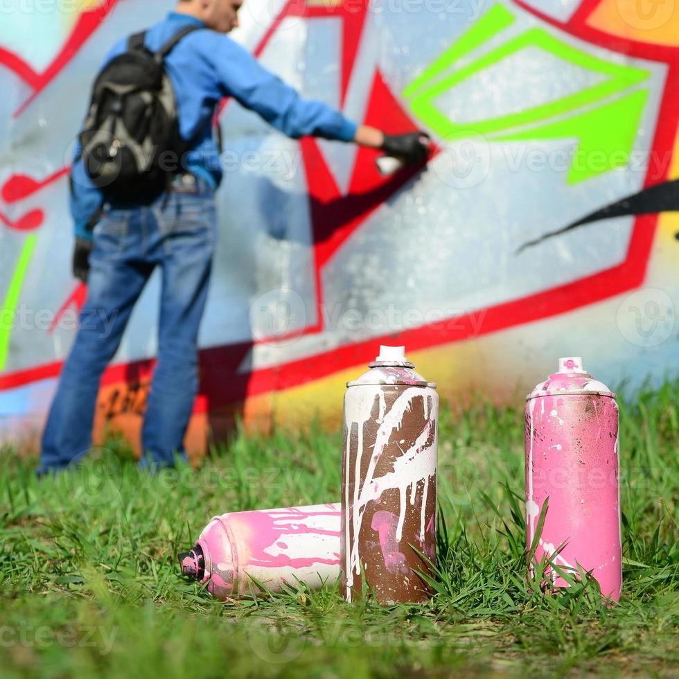 en få Begagnade måla burkar mot de bakgrund av de Plats med de vägg på som de ung kille drar en stor graffiti teckning. modern konst av teckning väggar i graffiti foto