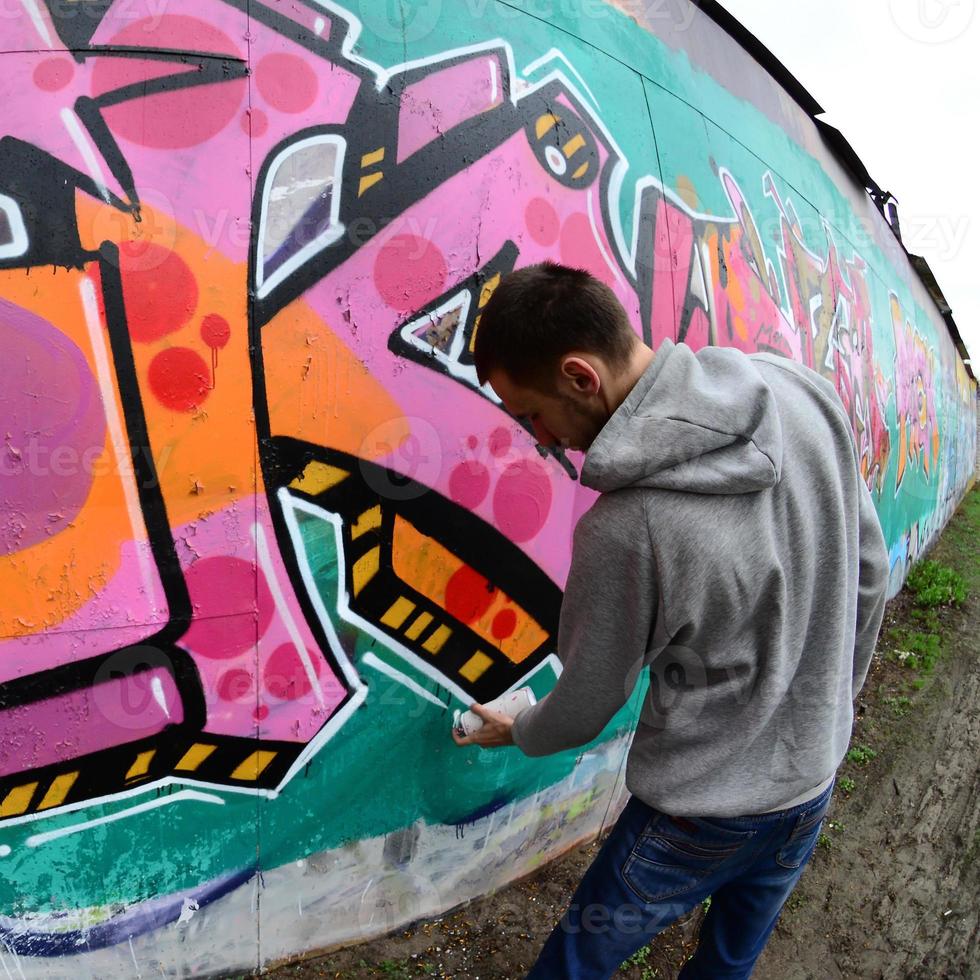 en ung kille i en grå luvtröja målarfärger graffiti i rosa och grön c foto