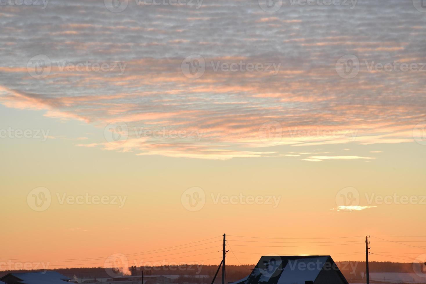 solnedgång landskap i de landsbygden i vinter. de miljö Sol Bakom de tak av de hus i de kväll. de disk av de Sol och de kväll solnedgång. gul rosa skön solnedgång och himmel. foto