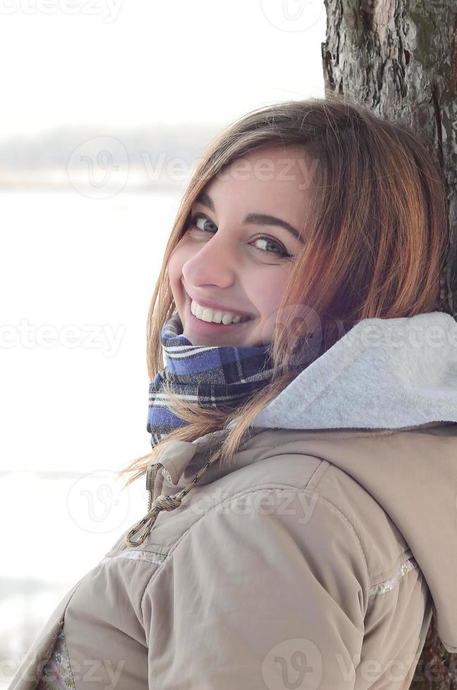 en ung och leende caucasian flicka utseende runt om de horisont linje mellan de himmel och de frysta sjö i vinter- tid foto