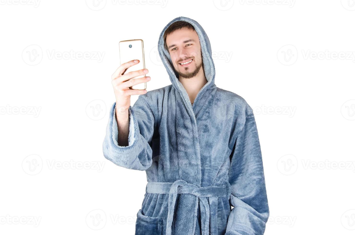 porträtt av ung caucasian skäggig man i blå morgonrock tar Foto med smartphone isolerat på vit bakgrund