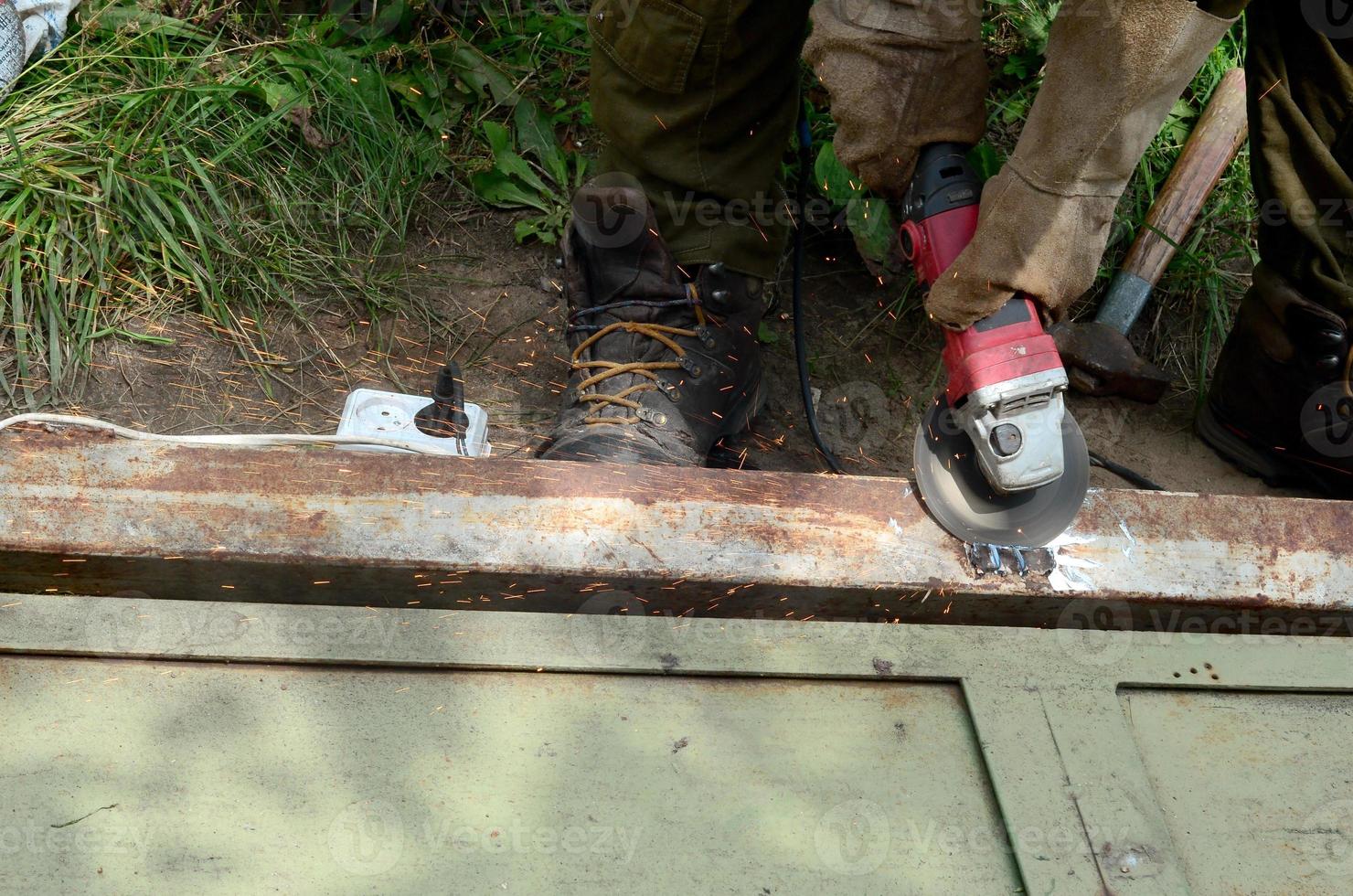 elektrisk hjul slipning på stål strukturera utomhus. gammal manuell arbetstagare i skyddande handskar skärande metall dörr med kvarn foto