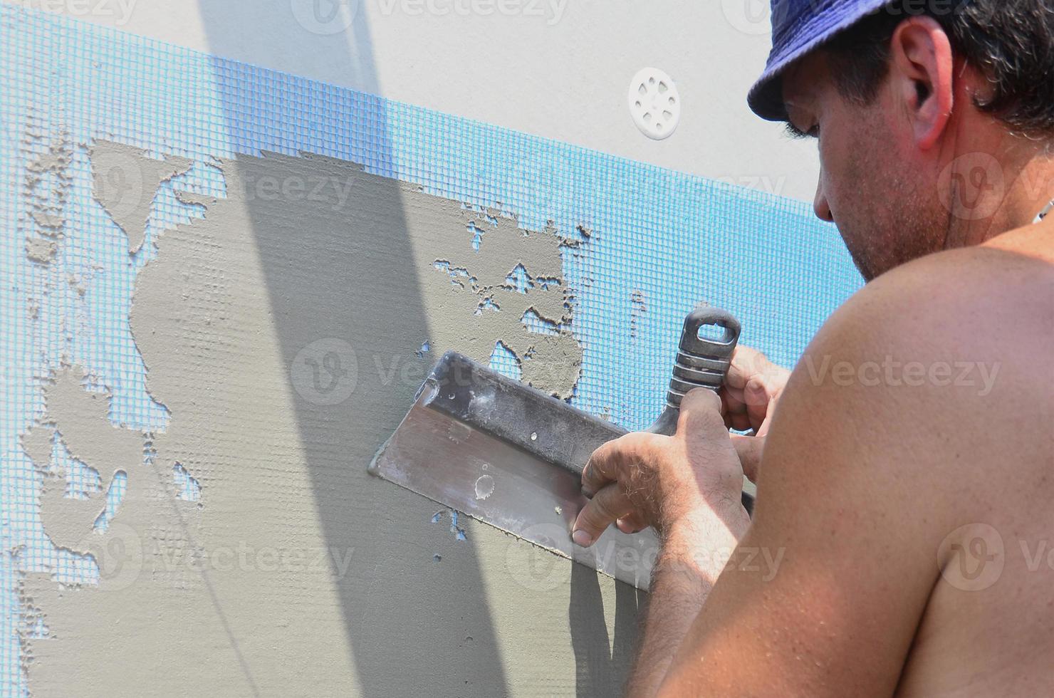 femtio år gammal manuell arbetstagare med vägg putsning verktyg renovera hus. murare renovera väggar och hörn med spatel och plåster. vägg mosa installation. konstruktion efterbehandling Arbetar foto