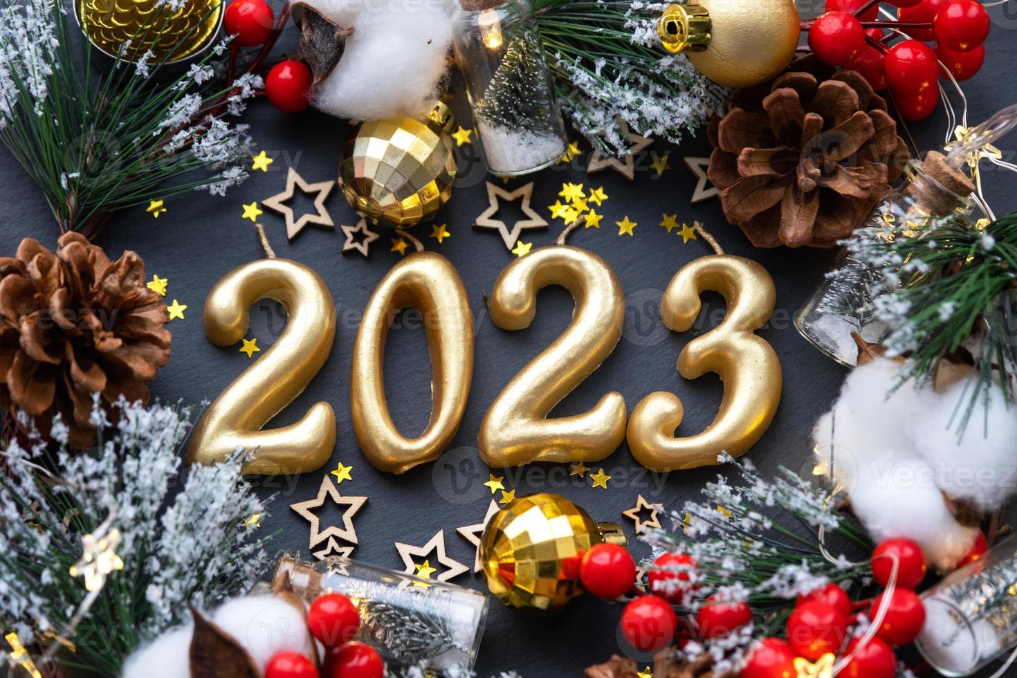 de gyllene siffror 2023 tillverkad av ljus på en svart sten skiffer bakgrund är dekorerad med en festlig dekor av stjärnor, paljetter, gran grenar, bollar och girlanger. hälsning kort, Lycklig ny år. foto