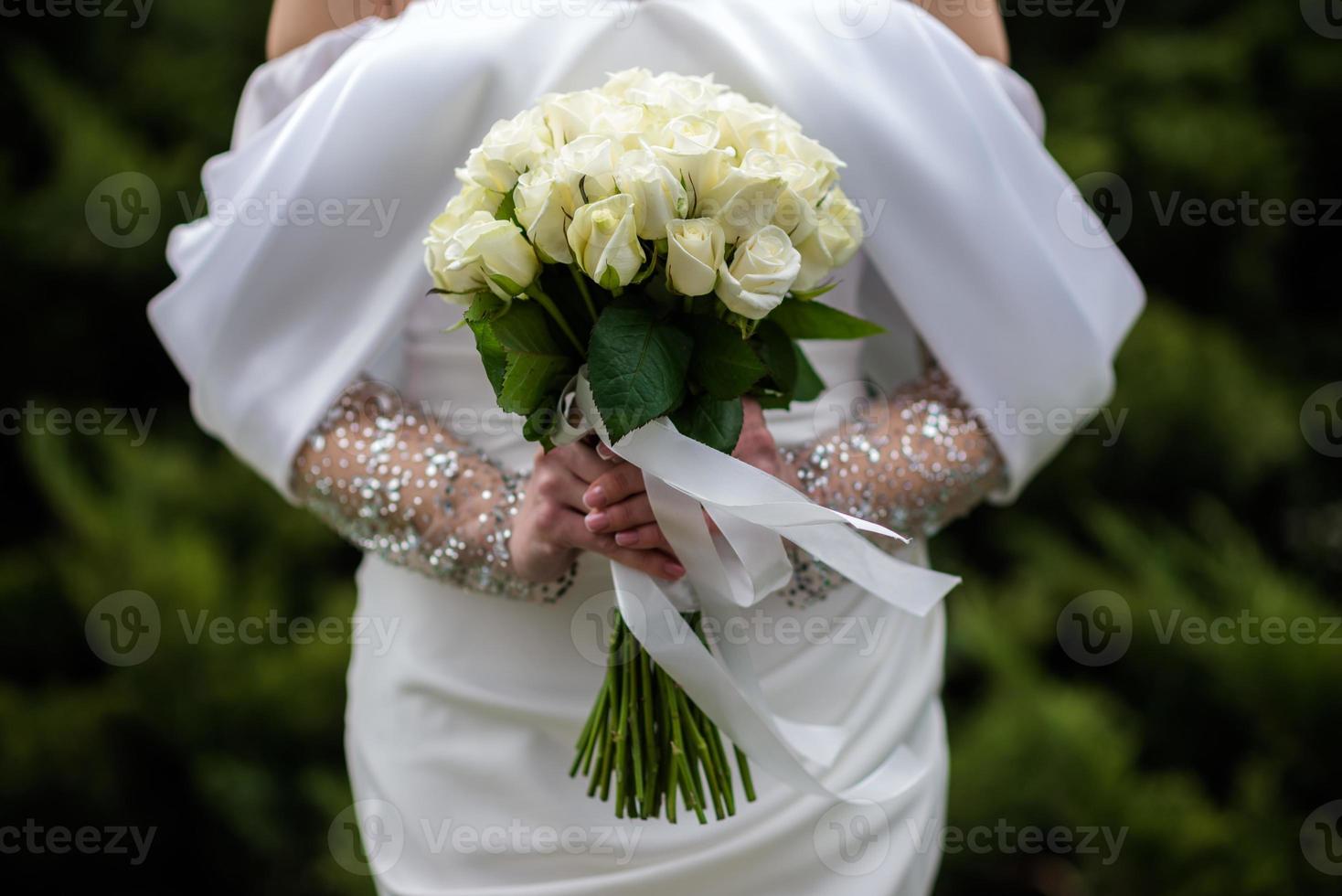 de brud i en vit bröllop klänning är innehav en bukett av vit blommor - pioner, rosor. bröllop. brud och brudgum. delikat Välkommen bukett. skön dekoration av bröllop med löv foto