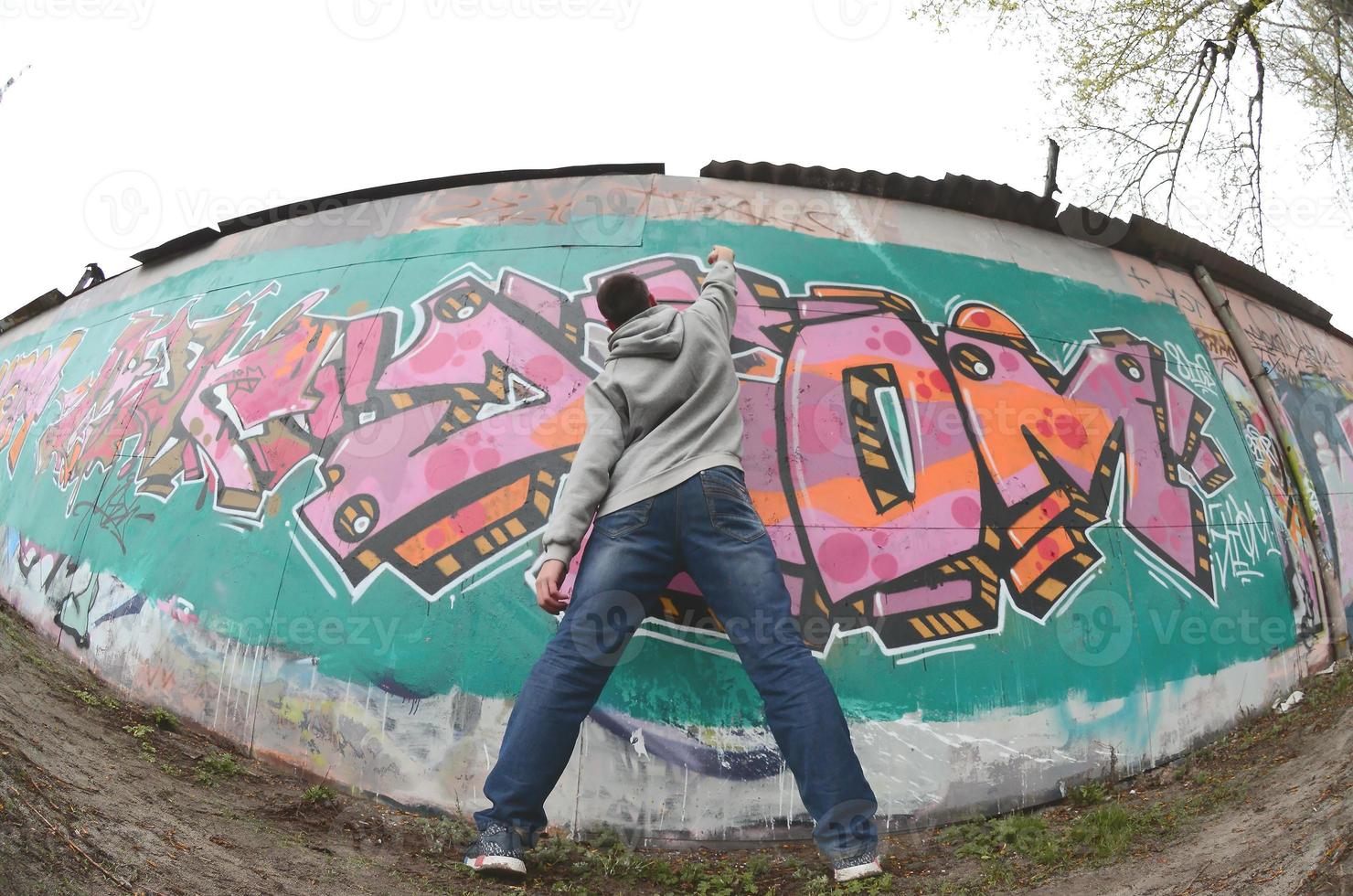 en ung kille i en grå luvtröja målarfärger graffiti i rosa och grön c foto