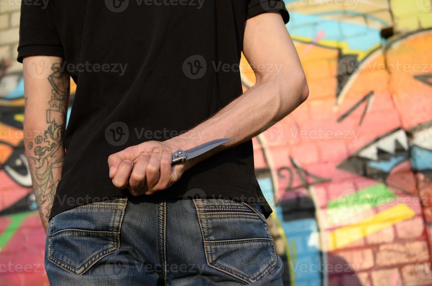 tillbaka se av ung caucasian man med kniv i hans hand mot getto tegel vägg med graffiti målningar. begrepp av kriminell krafter och aggression avgift foto