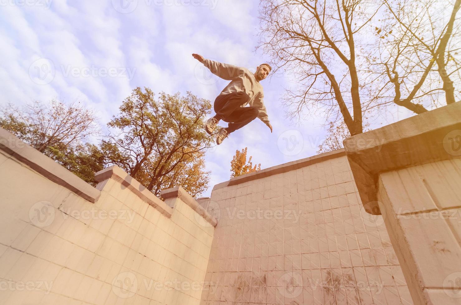 en ung kille utför en hoppa genom de Plats mellan de betong räcken. de idrottare praxis parkour, Träning i gata betingelser. de begrepp av sporter subkulturer bland ungdom foto