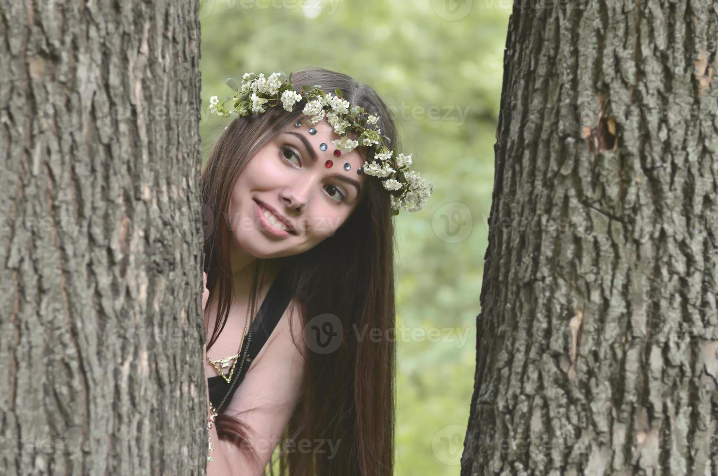 en skog bild av en skön ung brunett av europeisk utseende med mörk brun ögon och stor mun. på de flickans huvud är bär en blommig krans, på henne panna skinande dekorationer foto