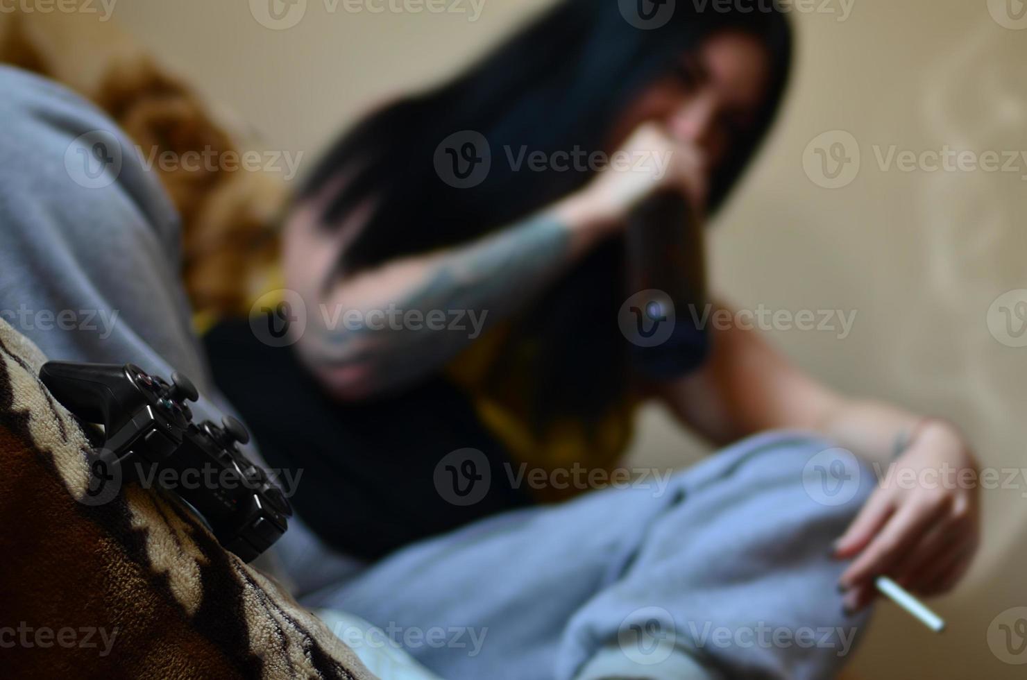 en flicka Sammanträde på de soffa, rökning en cigarett, dricka öl foto