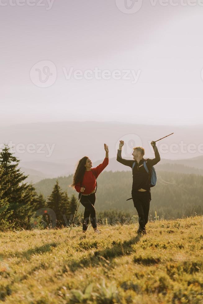 le par som går med ryggsäckar över gröna kullar foto