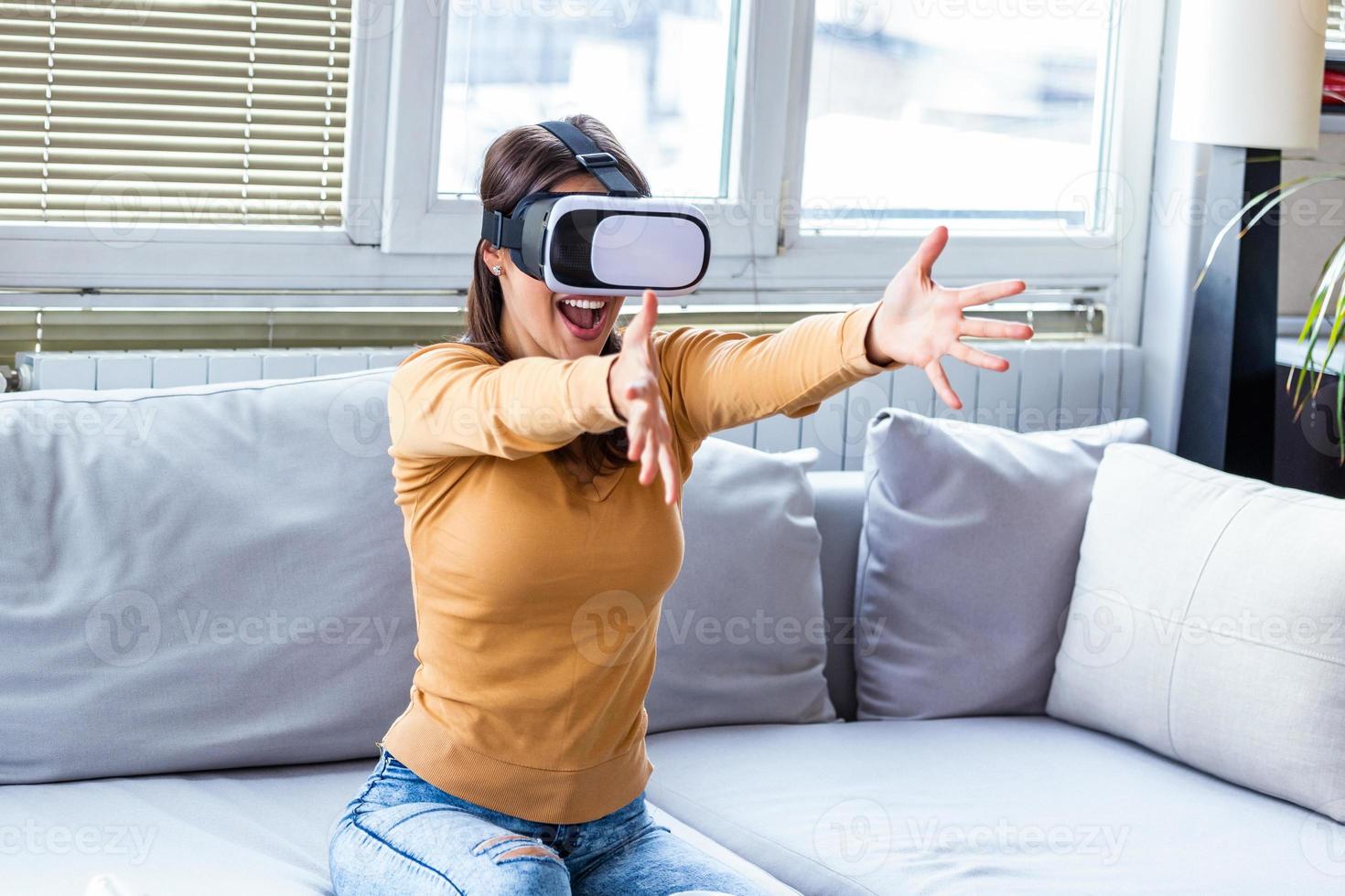 leende Lycklig kvinna få erfarenhet använder sig av vr-headset glasögon av virtuell verklighet på Hem. Lycklig förvånad ung kvinna med virtuell verklighet headsetet eller 3d glasögon Sammanträde på soffa på Hem foto