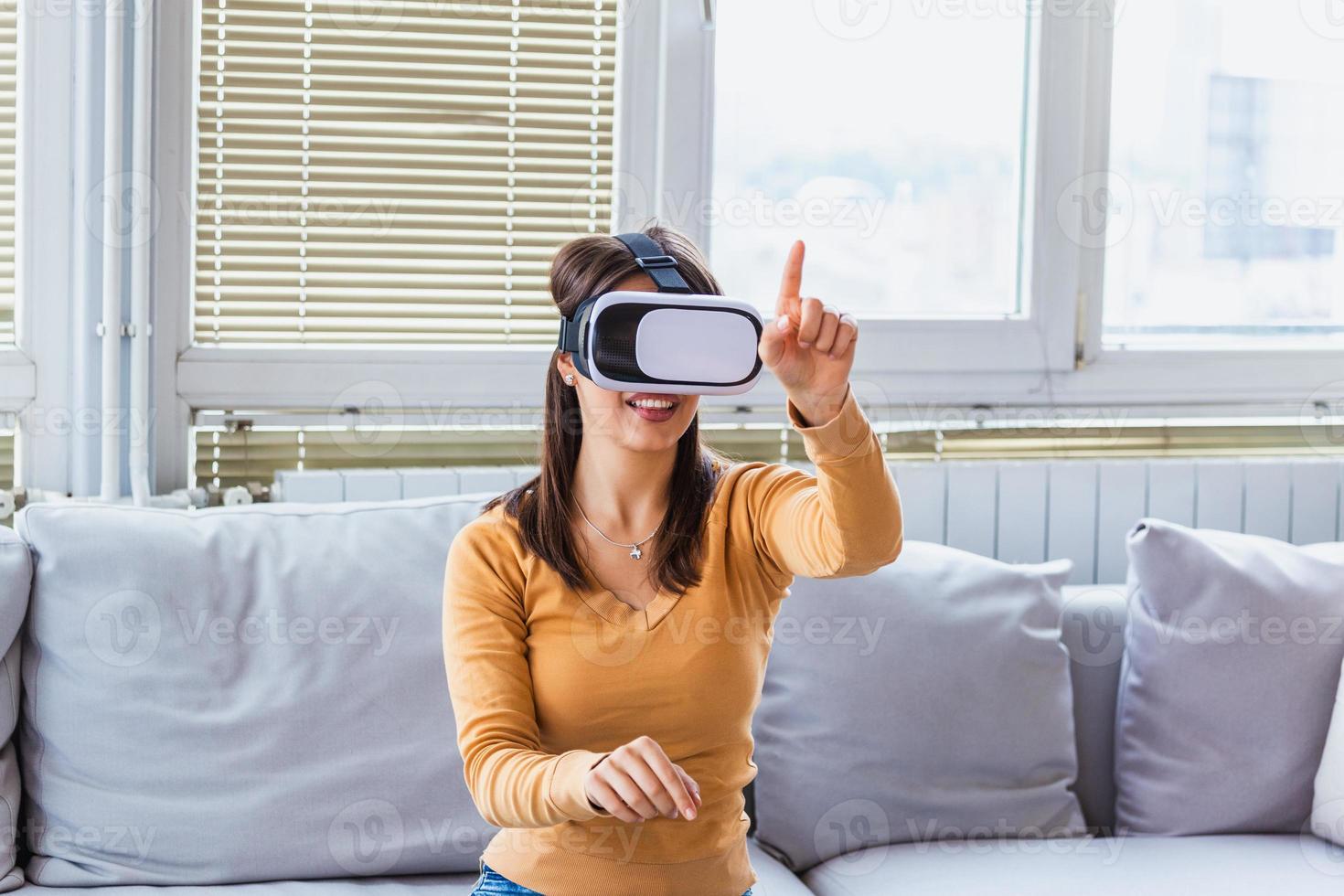 glad flicka med händer upp bär de virtuell verklighet glasögon. kvinna njuter virtuell verklighet på Hem. skön kvinna bär vr virtuell verklighet headsetet med gränssnitt. foto