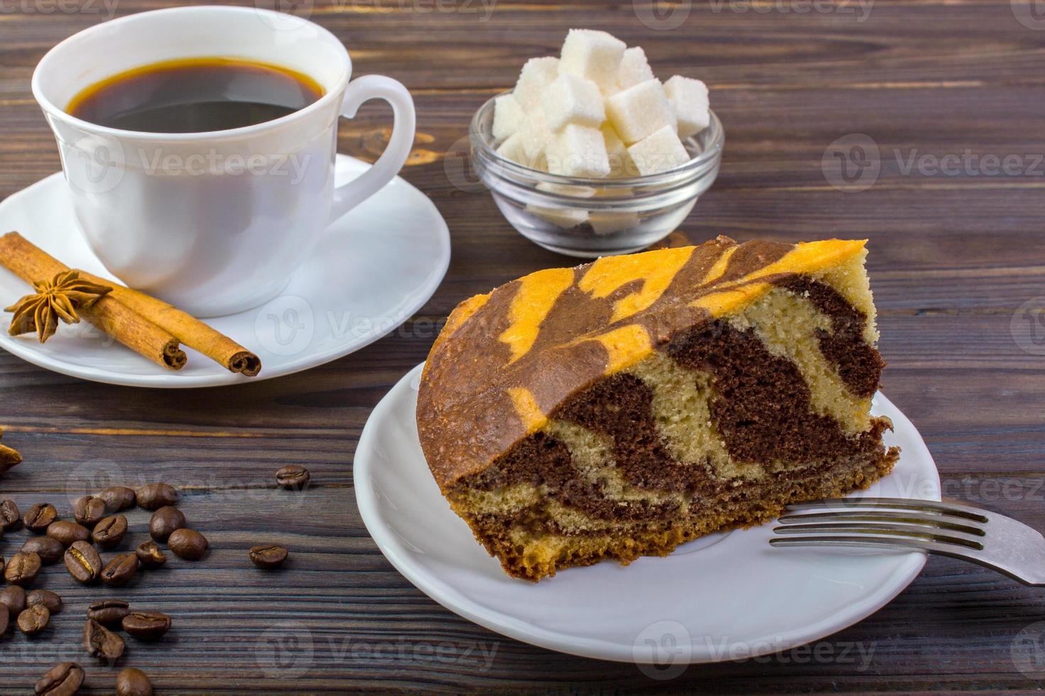 utsökt kaka på en tallrik med en gaffel. vit kopp med svart kaffe och kanel pinnar nära Det. kaffe bönor och en skål med socker kuber på mörk trä- tabell foto