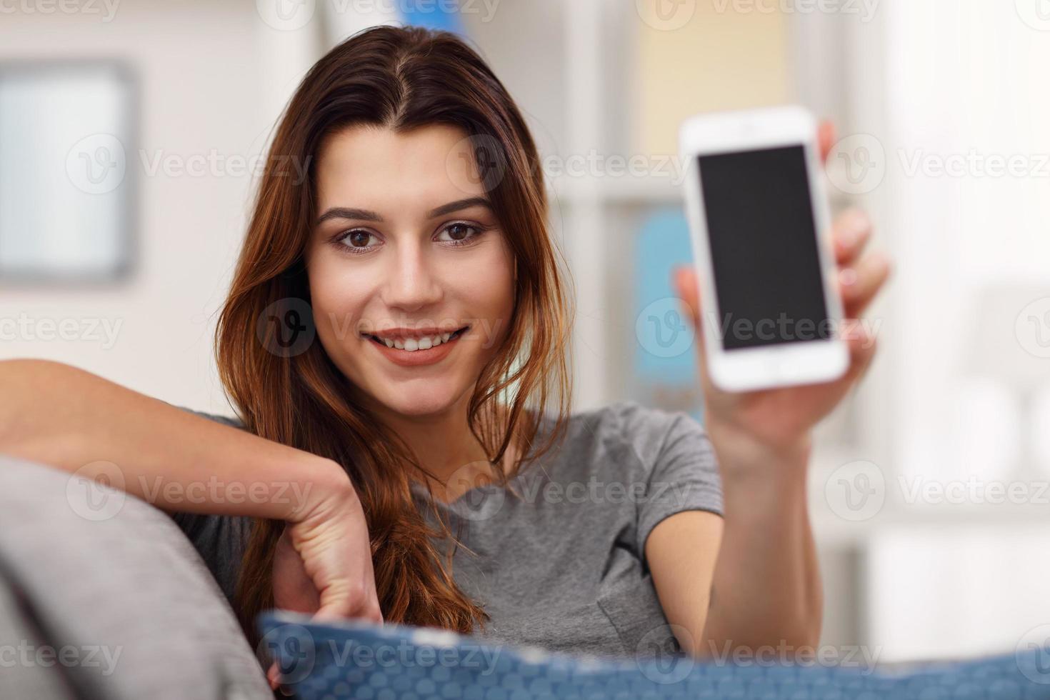 Lycklig vuxen kvinna använder sig av telefon på Hem i de levande rum foto