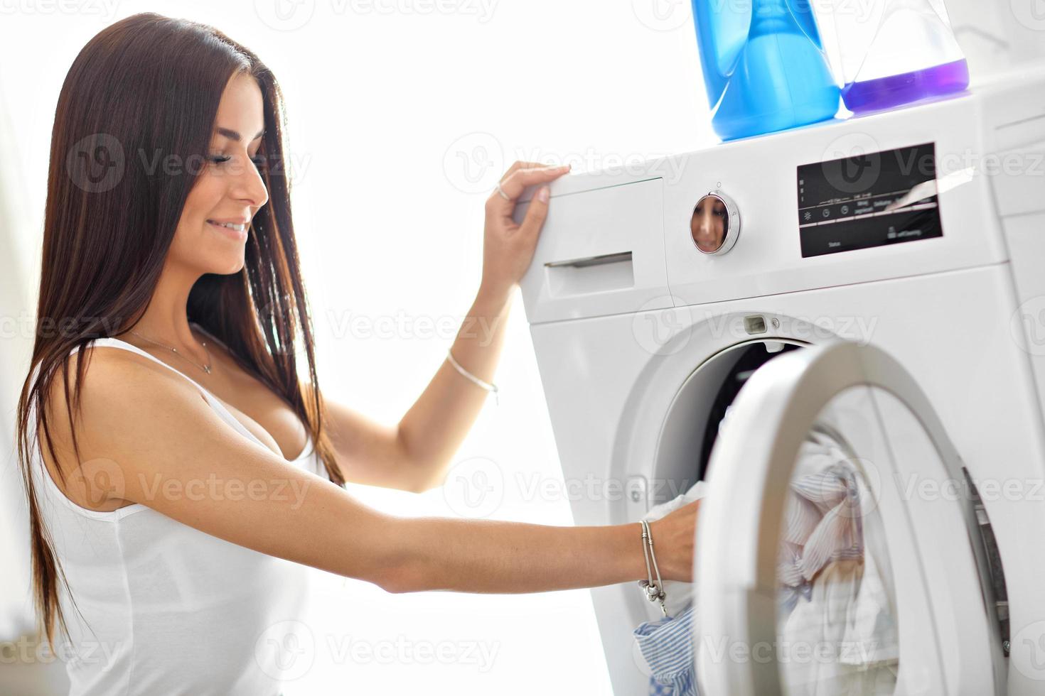porträtt av ung hemmafru med tvätt Nästa till tvättning maskin foto