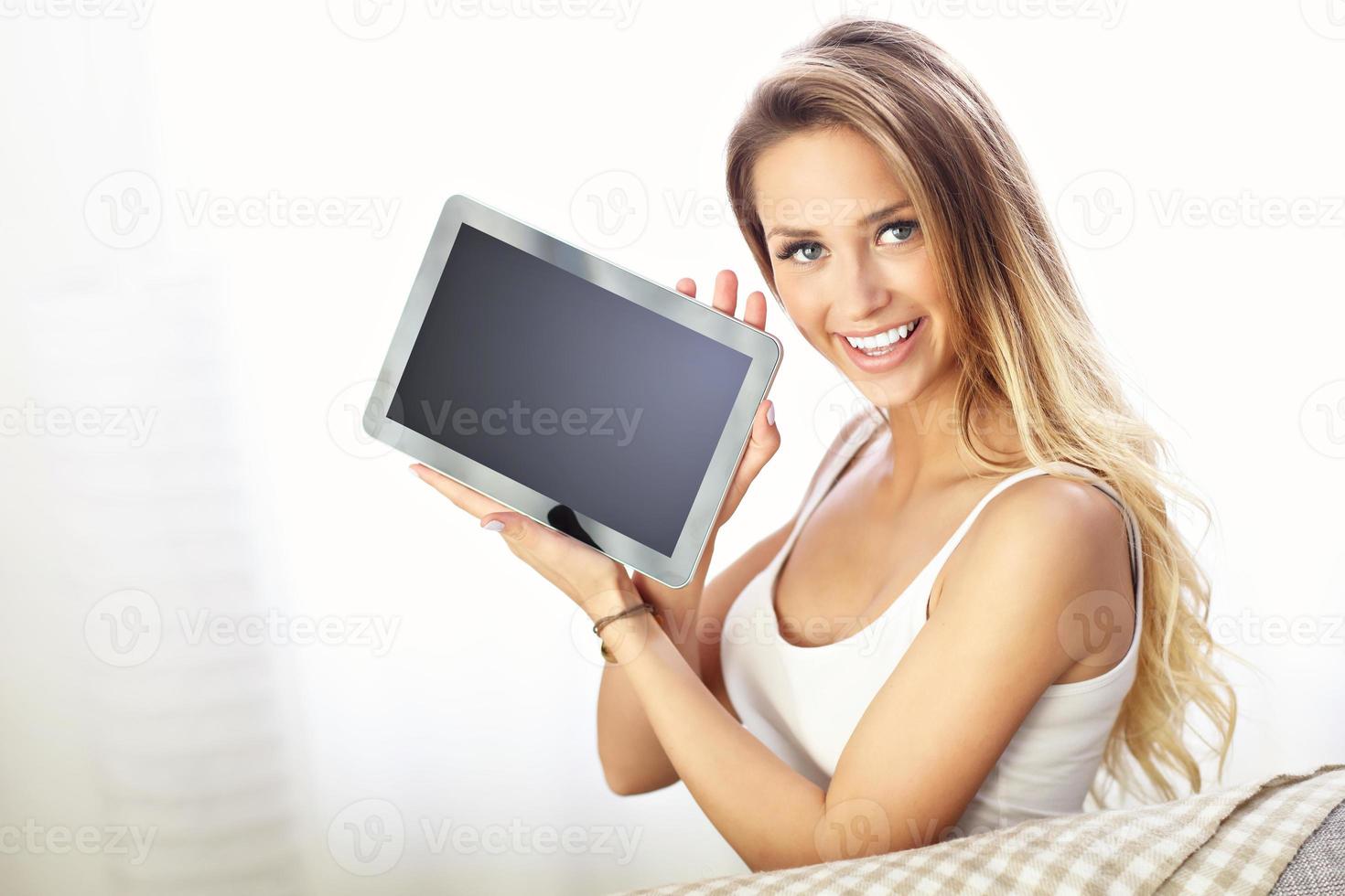Lycklig kvinna med läsplatta på soffa foto