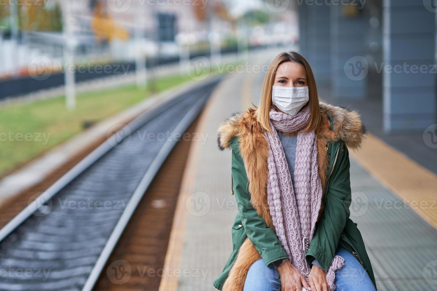 vuxen kvinna på tåg station bär masker på grund av till covid-19 restriktioner foto