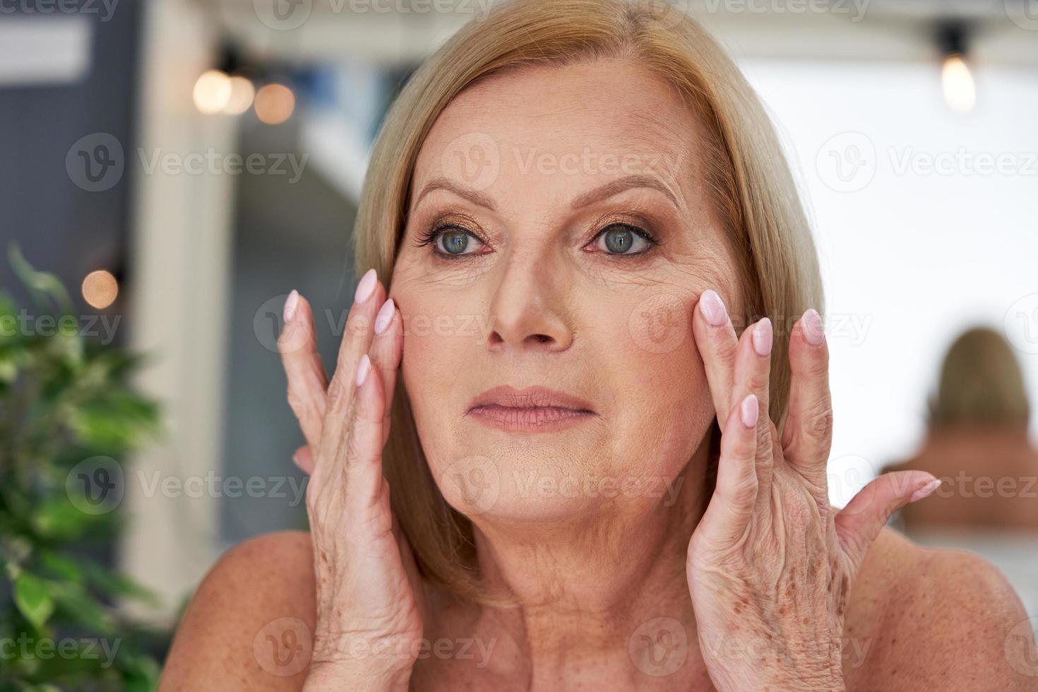 senior kvinna använder sig av anti skrynkla grädde i de badrum foto