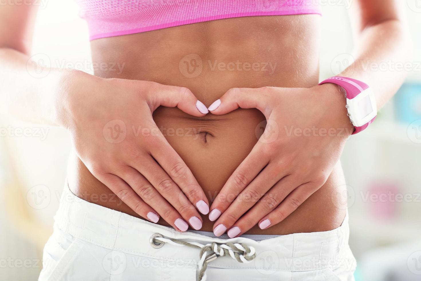 närbild av ung kvinna framställning hjärta form med henne händer på henne mage foto