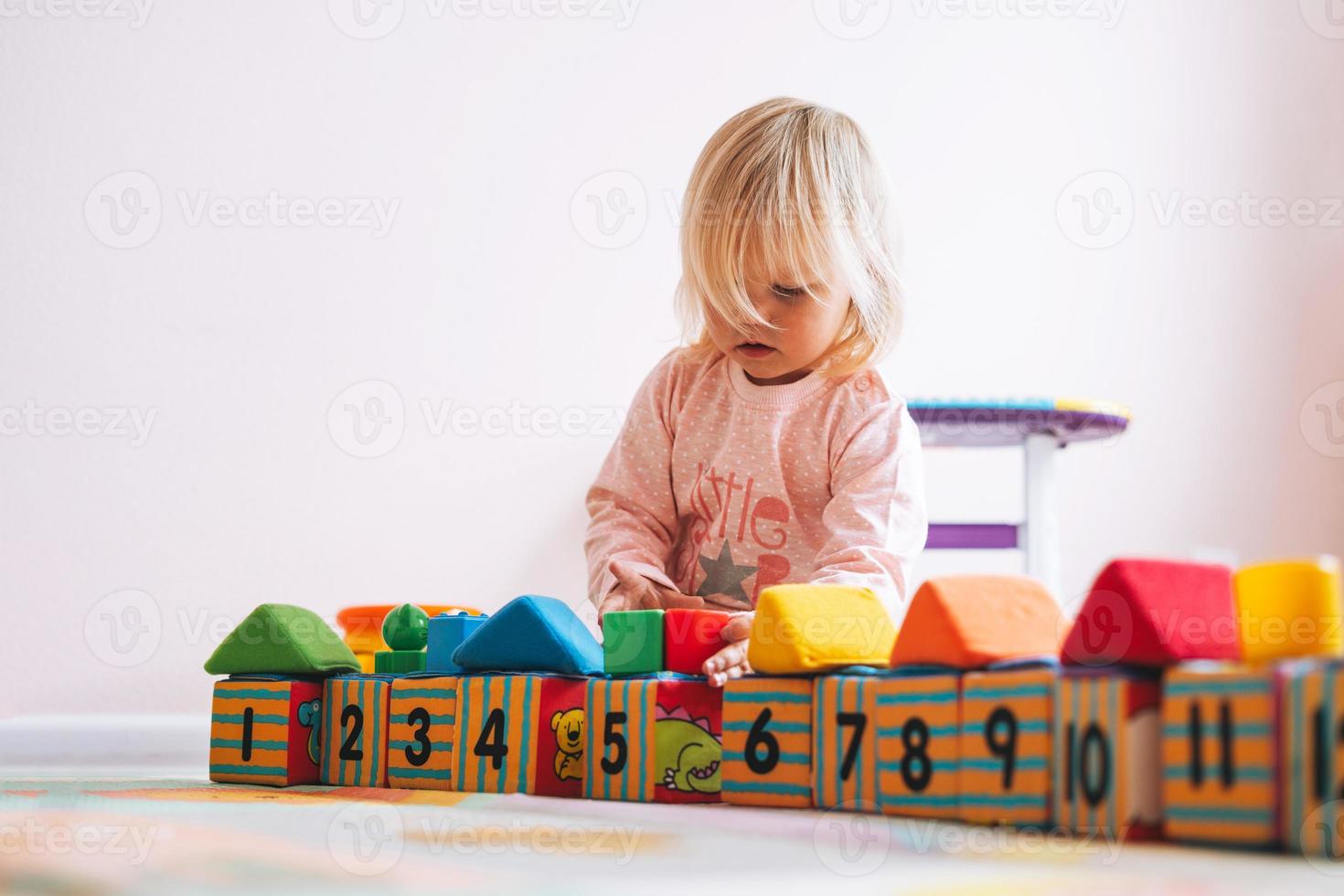 liten flicka litet barn i rosa spelar med block med tal i barns rum på Hem foto