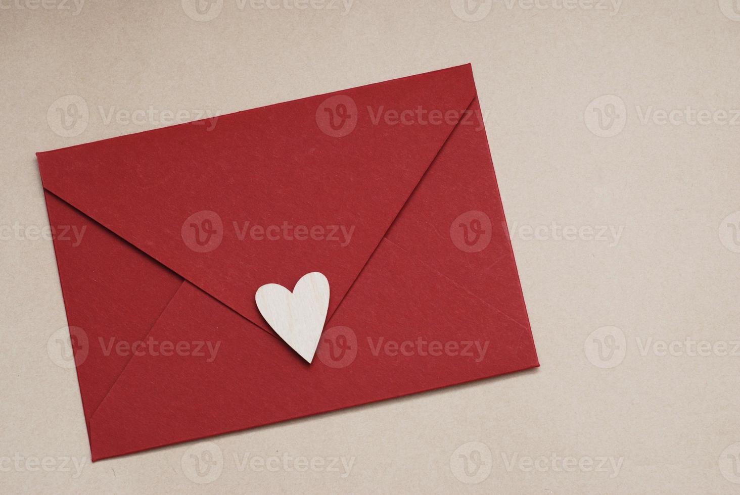 närbild av röd papper kuvert med vit hjärta på neutral brun bakgrund. kärlek och hjärtans dag begrepp. foto