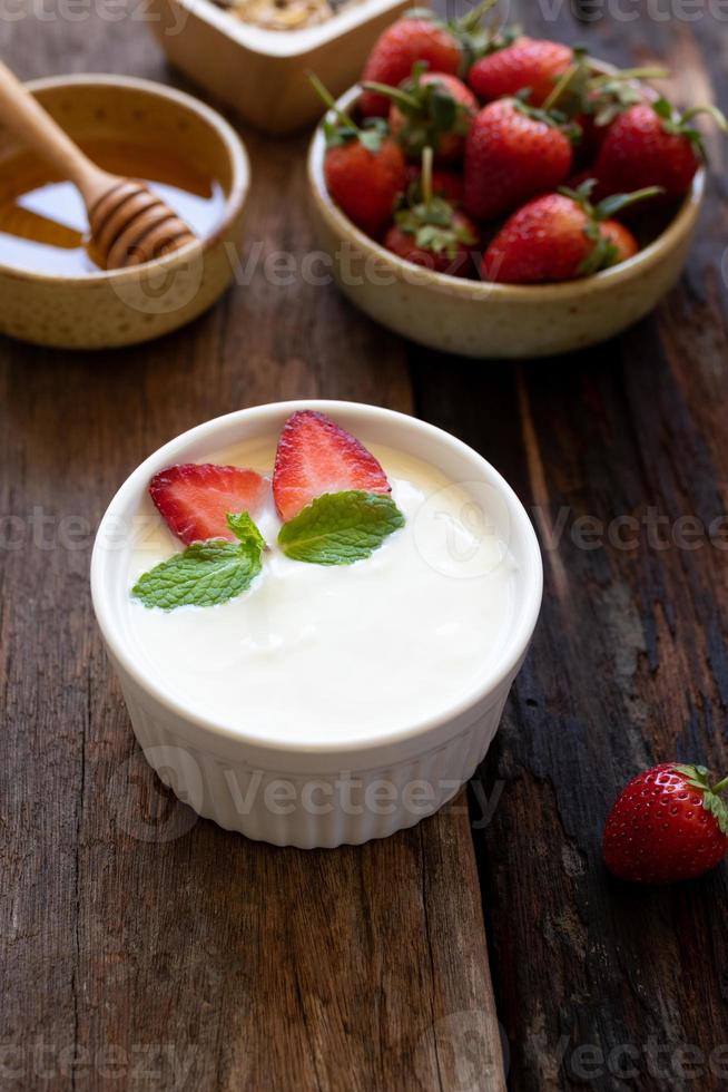 jordgubb yoghurt i en trä- skål med granola, honung, mynta och färsk jordgubb på trä- bakgrund. hälsa mat begrepp. foto