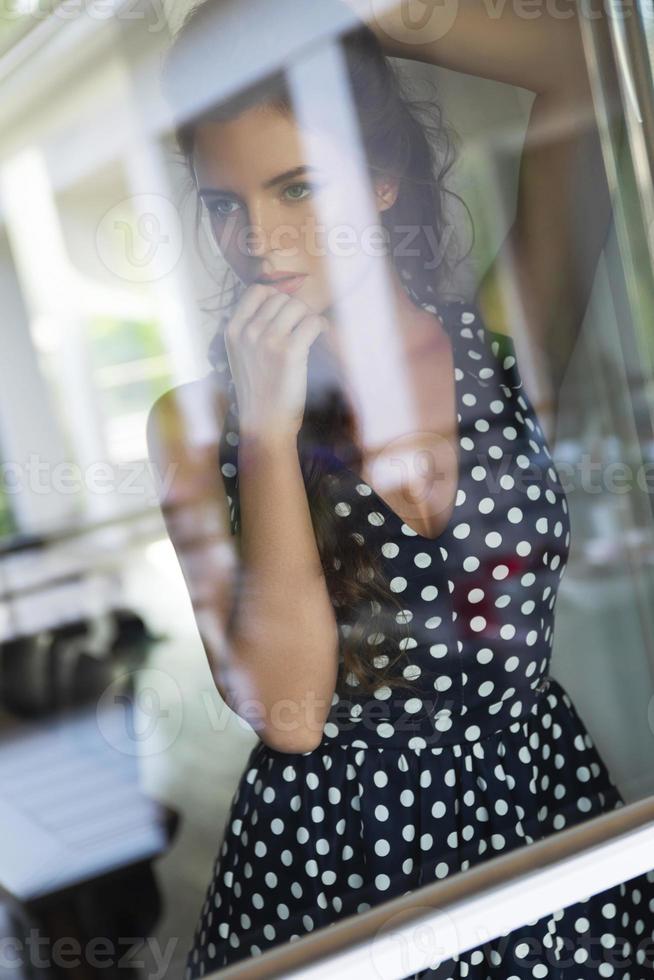 underbar kvinna bär skön klänning med en polka punkt mönster ser genom de fönster foto