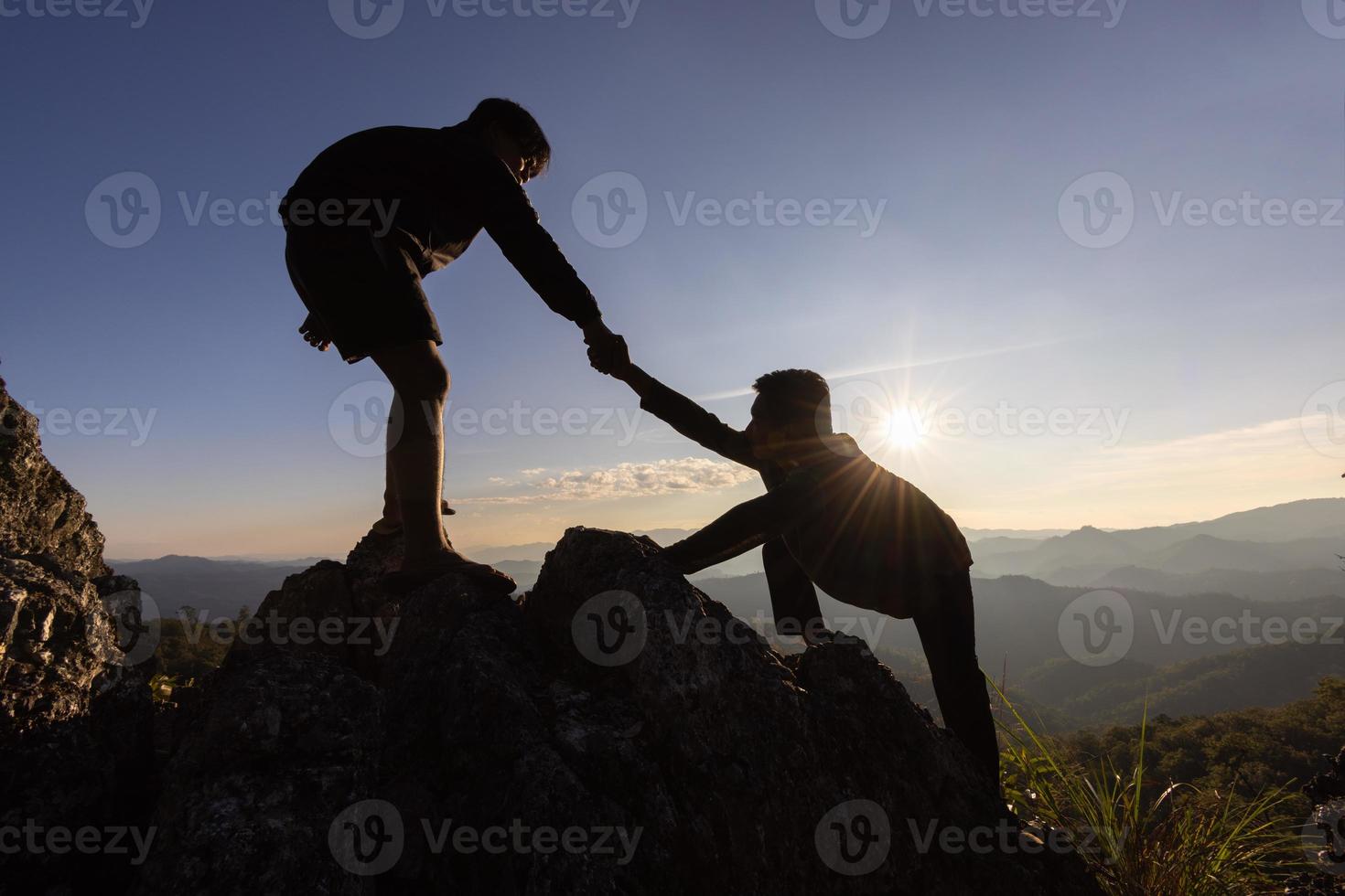 silhuett av portion hand mellan två klättrare. par vandring hjälp varje Övrig silhuett i bergen med solljus. de män portion dra människor upp från hög klippor foto