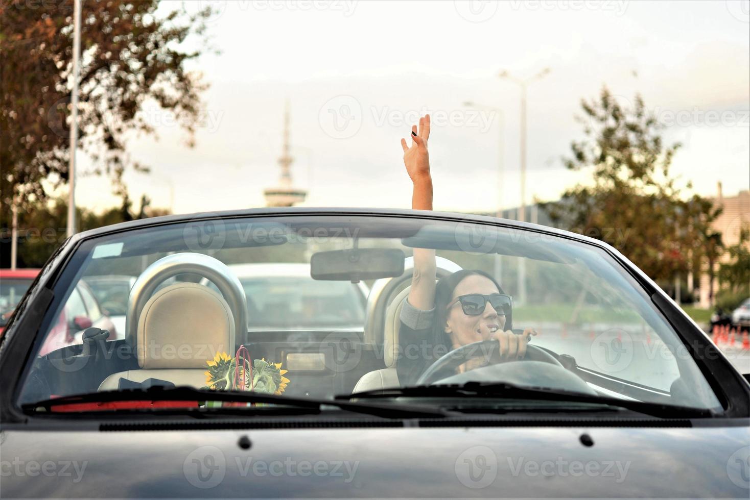 Lycklig skön kvinna körning en sporter konvertibel bil i de stad foto