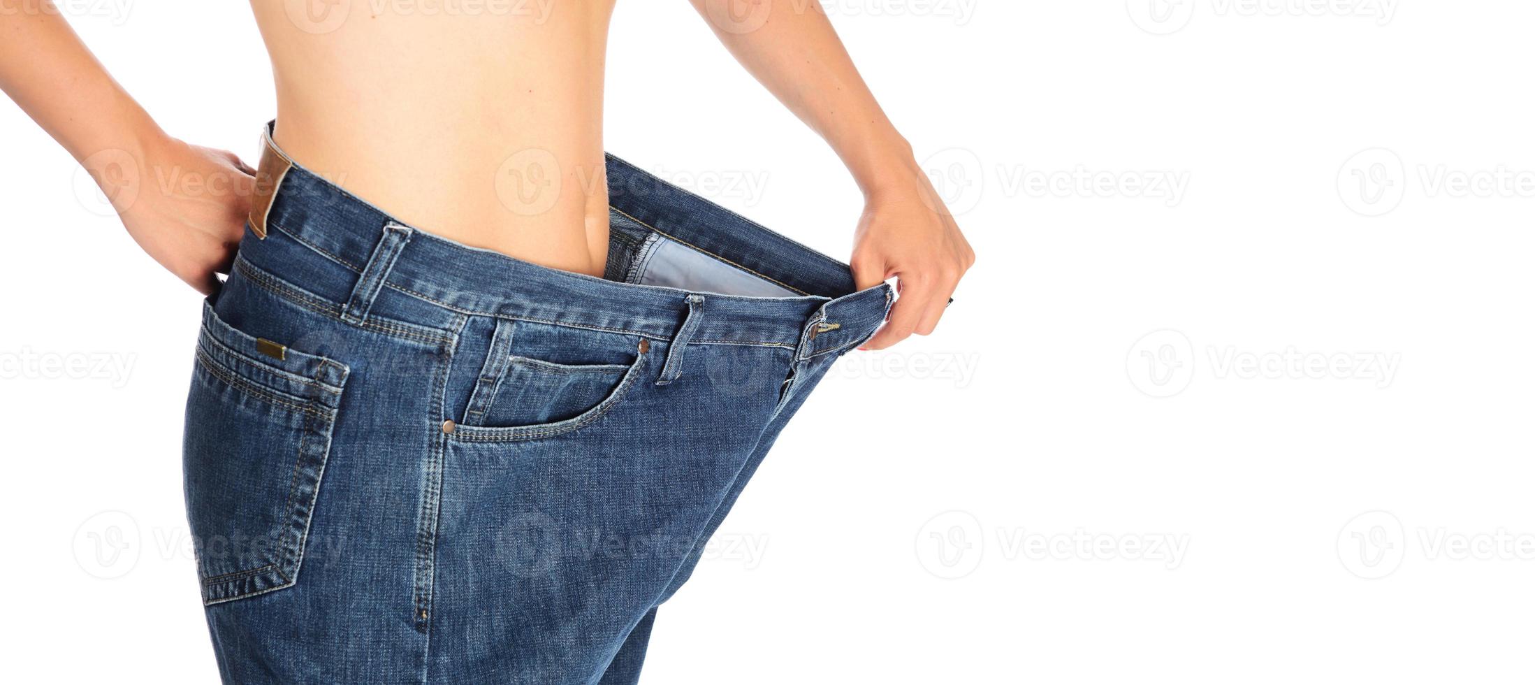 mitten sektion av en kvinna med mage fett innehav henne blå jeans. flicka med stor jeans isolerat på vit bakgrund. kvinna visar henne vikt förlust. friska livsstil begrepp foto