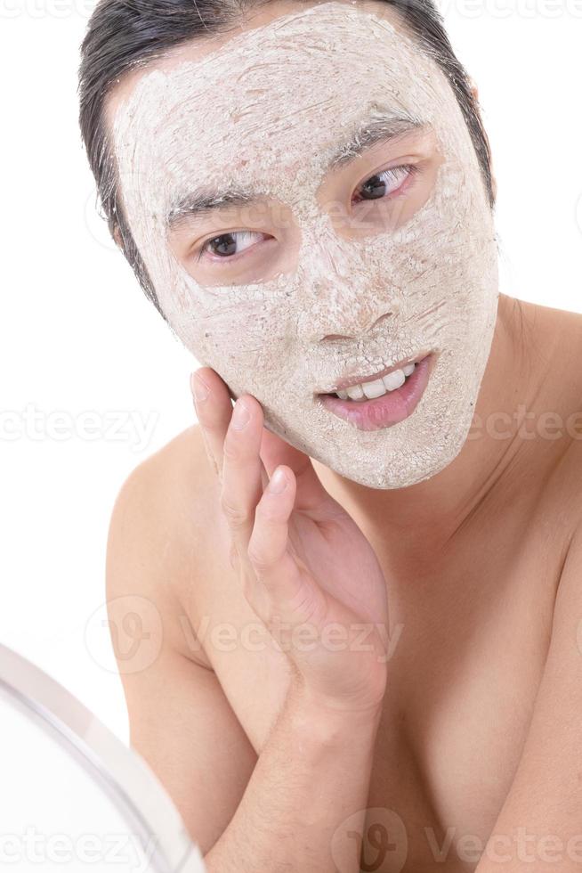 skönhet procedur och hud vård. stänga upp porträtt av Lycklig skrattande topless asiatisk man med ansikte mask rörande hans ansikte. isolerat på vit bakgrund. foto