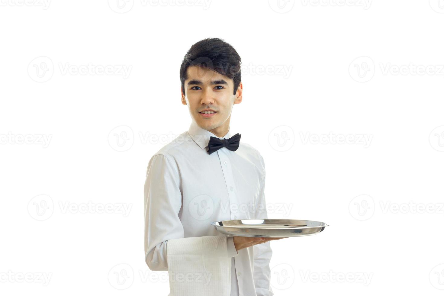 ung söt servitör utseende framåt- till leende och innehav en handduk med en bricka foto