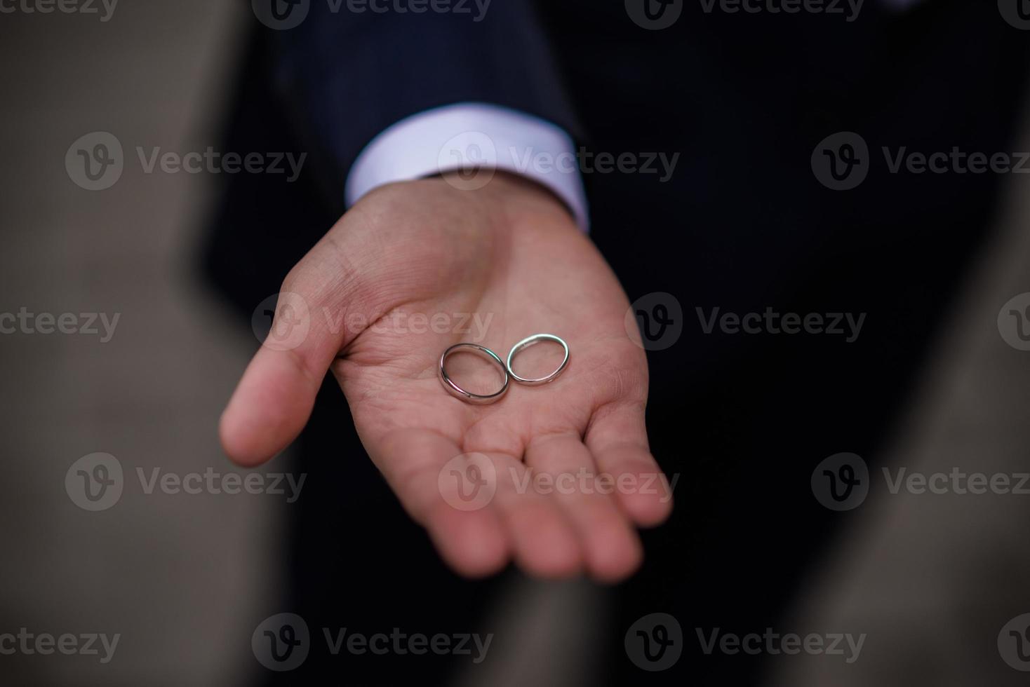 brudgum innehav bröllop ringar i hand. två bröllop ringar på de golv med kontrast bröllop ringar på golv, på jord, på piano, i hand foto