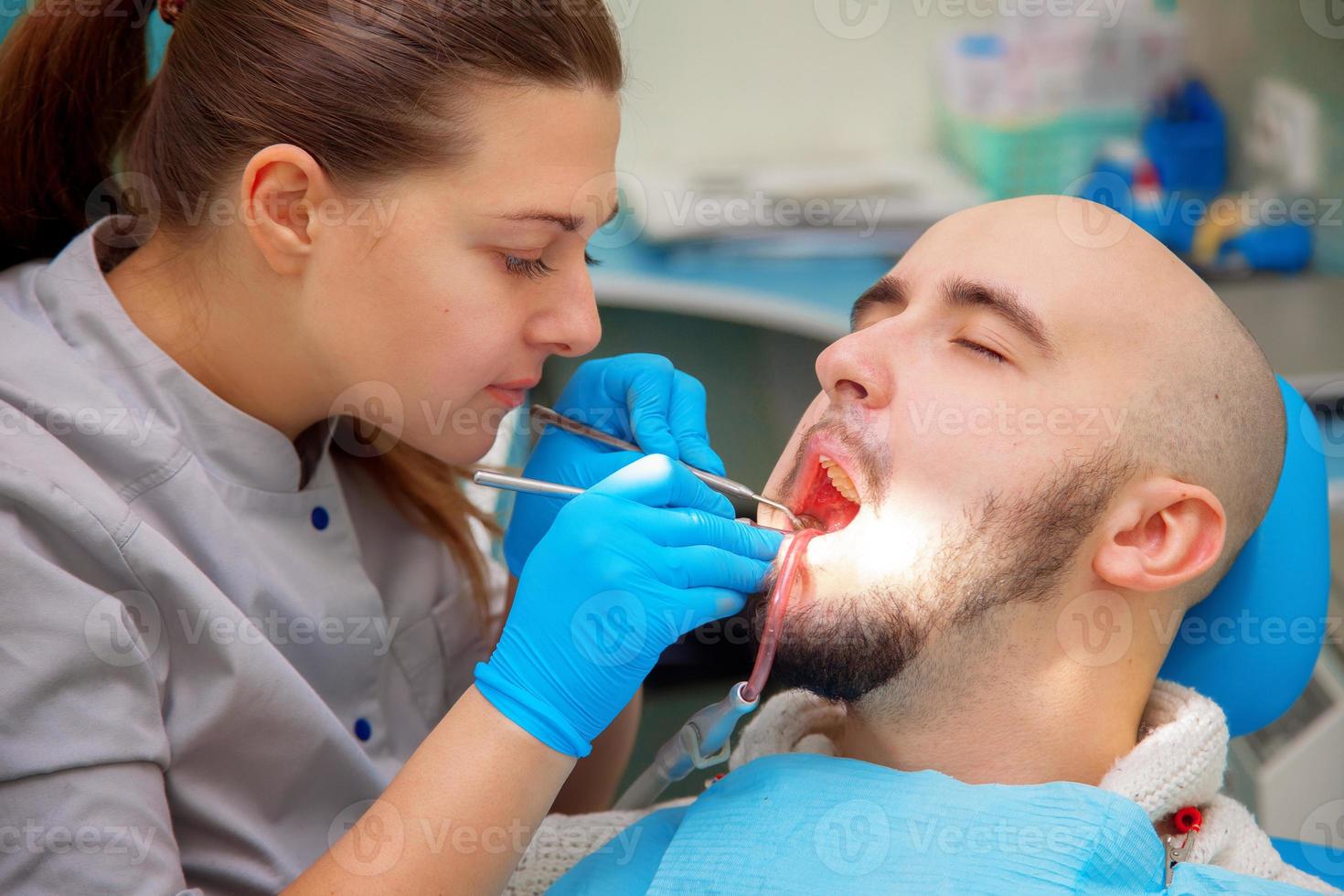 tandläkare granskning en patienter tänder i de tandläkare stol under ljus ljus på de dental klinik foto