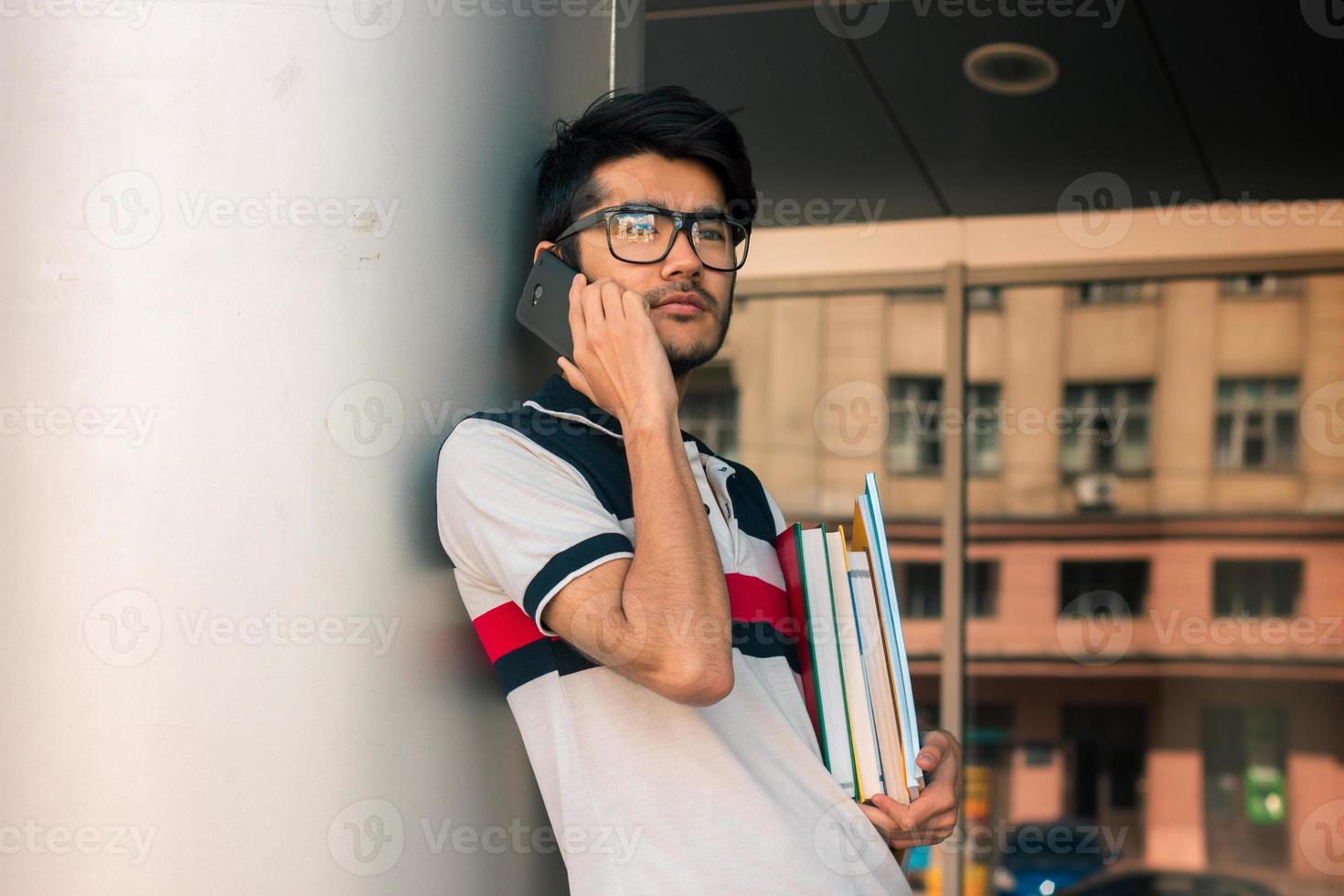 charmig kille i glasögon på de telefon och innehav en bok foto