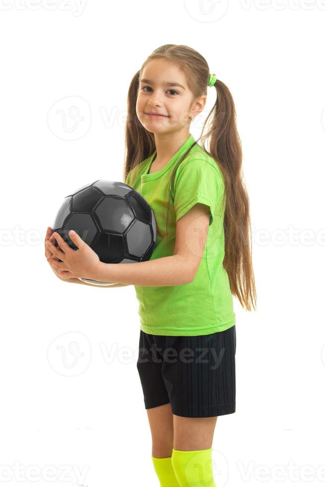 vertikal porträtt av sötnos liten flicka i grön skjorta innehav en fotboll boll i händer foto